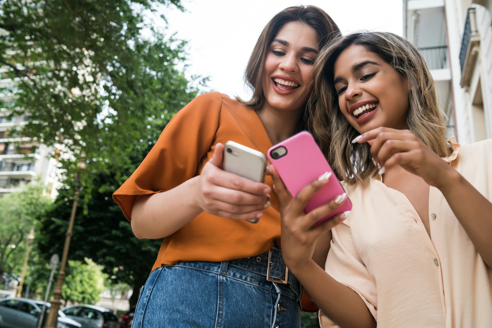 Two friends comparing phones outdoors, mid-conversation, neither blocked by a sign-in screen